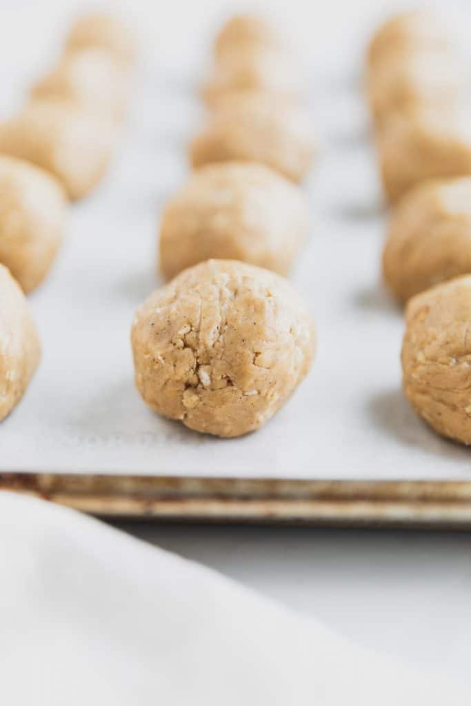 raw oatmeal cookie dough rolled into balls and lined up on a parchment paper lined baking sheet