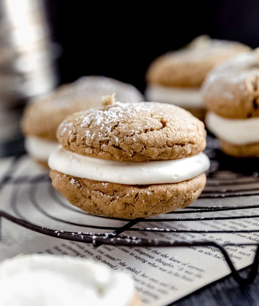 oatmeal cream pies on top of a circular cooling rack with book pages underneath and powdered sugar dusted on top