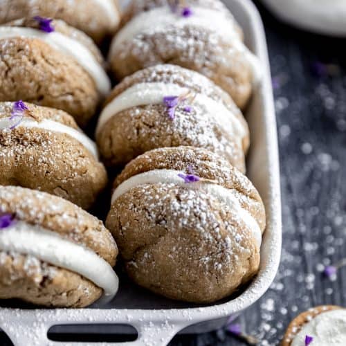 oatmeal cream pies in a white ceramic baking dish dusted with powdered sugar and pieces of lavender on a dark weathered wood surface