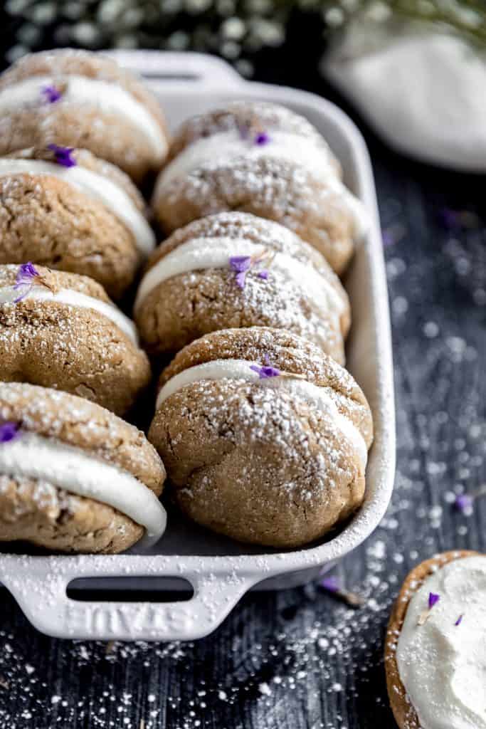 oatmeal cream pies in a white ceramic baking dish dusted with powdered sugar and pieces of lavender on a dark weathered wood surface