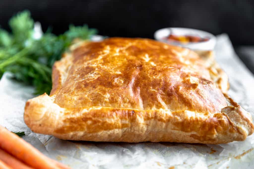 puff pastry fresh out of the oven dark golden brown on top of white parchment paper with carrots that have green tops sitting to the side