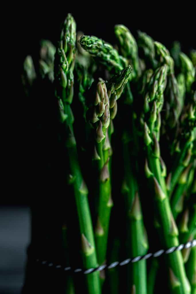 close up of a bundle of asparagus with shadows and a black background tied together by black and white twine