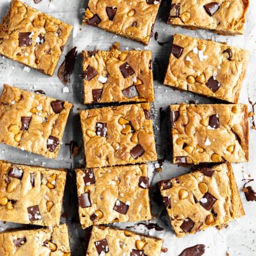 the best blondies with chocolate, butterscotch and toasted pecans spread out in rows on a white surface