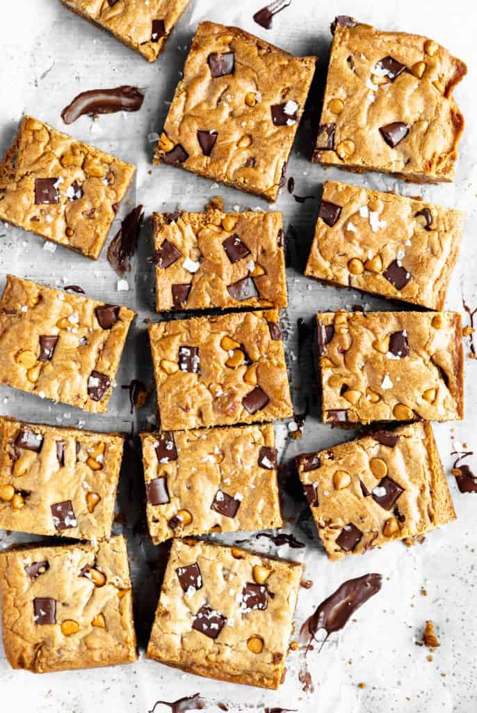 the best blondies with chocolate, butterscotch and toasted pecans spread out in rows on a white surface