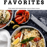 garlic chicken pasta in a bowl with a white linen next to it, a bowl of roasted tomatoes, lemon wedges and a microplane grater on a dark surface