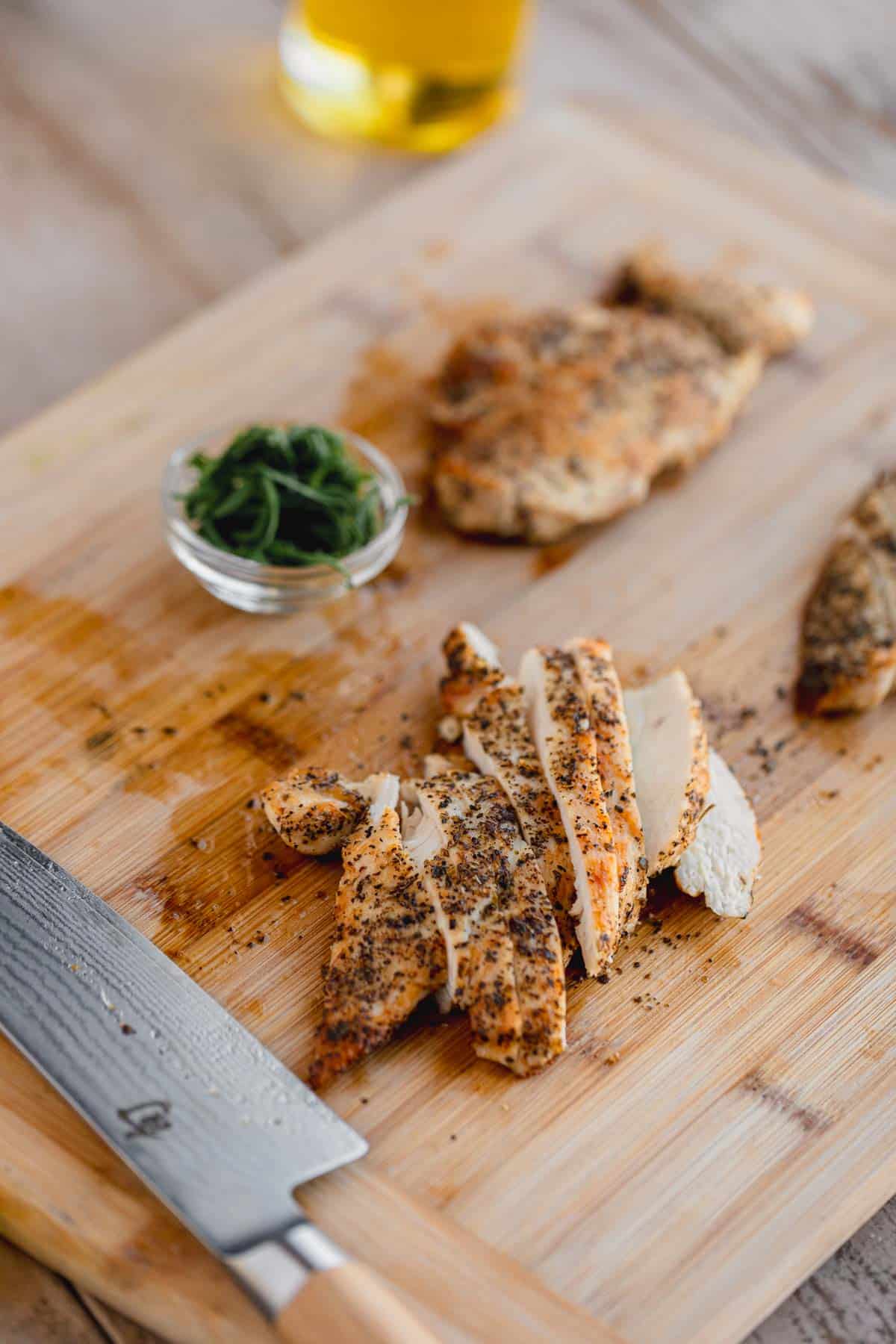 Sliced chicken on a cutting board with basil and a knife. 