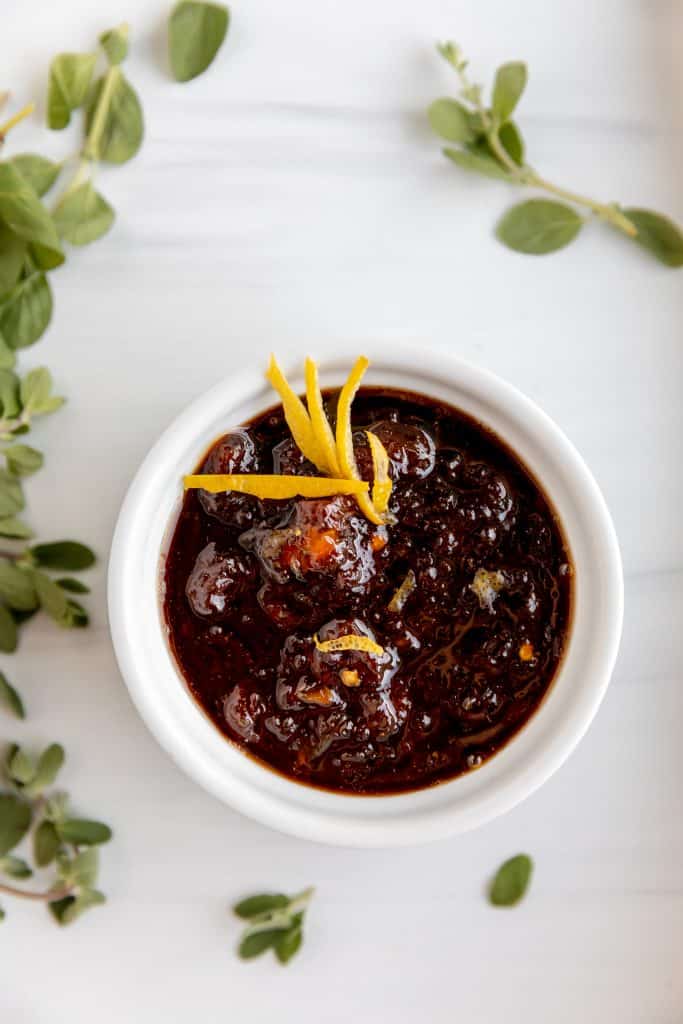 lemon chutney in a white dish with lemon zest on top and fresh oregano around the outsides of the bowl