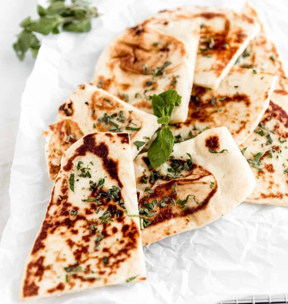 naan cut up into quarters on a sheet of parchment paper topped with fresh mint and oregano