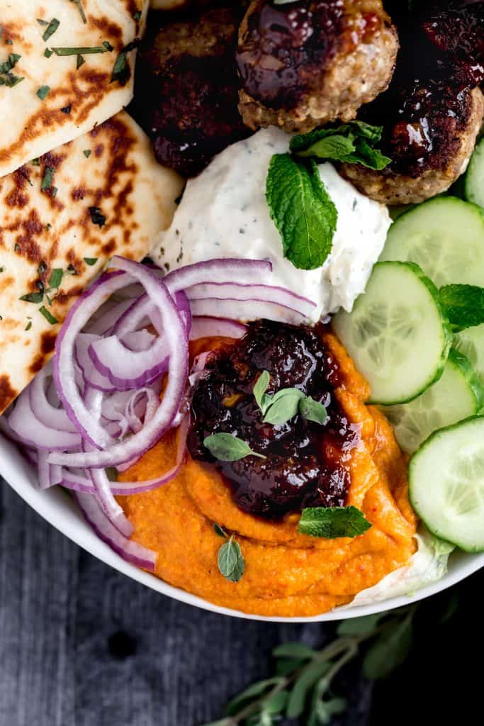 a close up shot of the lemon chutney sitting on tp of the cherry pepper hummus with veggies and naan surrounding it