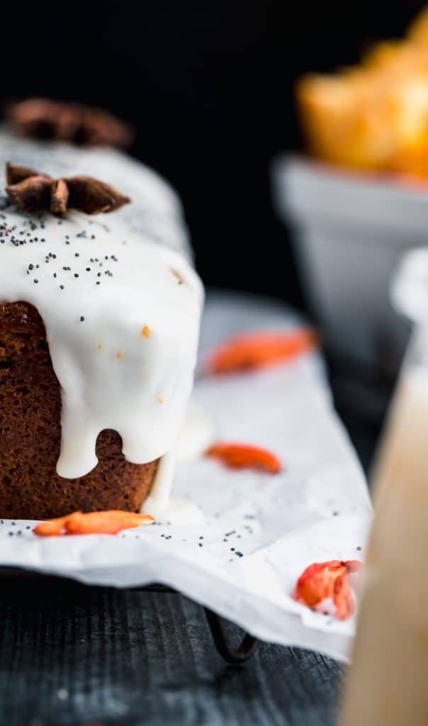 Straight on view of orang poppy seed bread with the yogurt drip coming down the side. topped with whole star anise and poppy seeds. dried orange flowers sitting on top of parchment paper