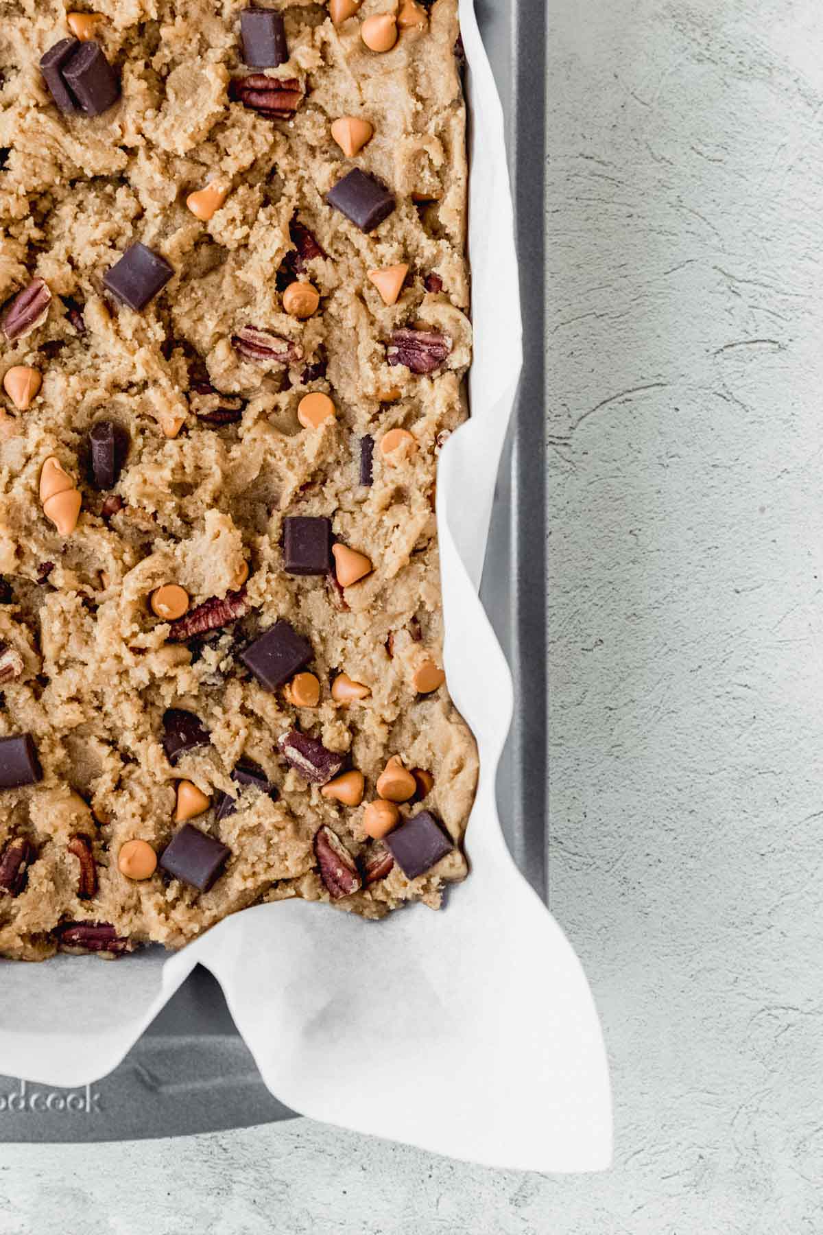 Blondie batter in a baking pan lined with parchment paper.