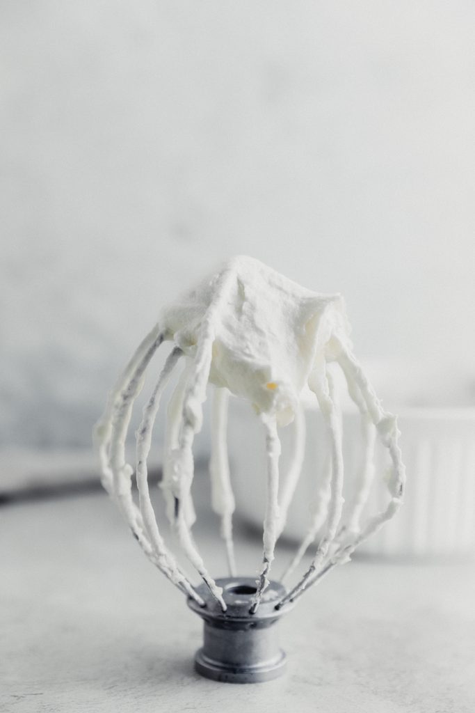 almond cream cheese frosting on a whisk attachment sitting upside down on a surface with a white bowl in the background