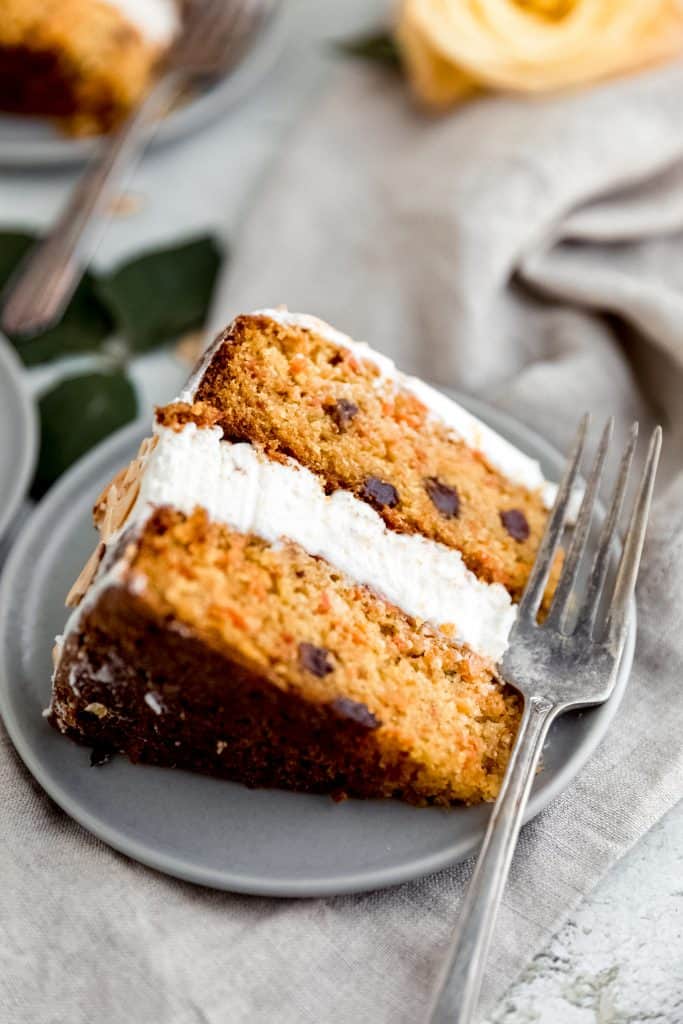 one slice of almond carrot cake sitting on a grey plate with a fork next to it sitting on a surface with a linen