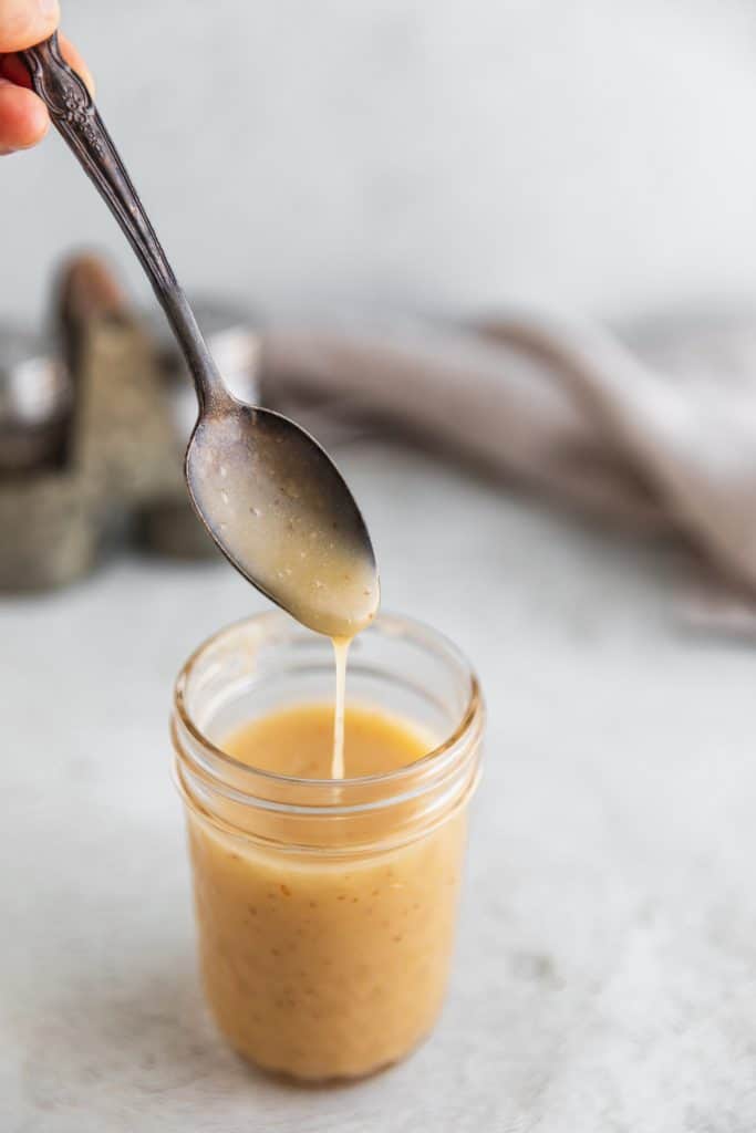 sherry vinaigrette in a clear  small ball jar sitting on the counter top with a spoon over the top drizzling the vinaigrette back into the jar