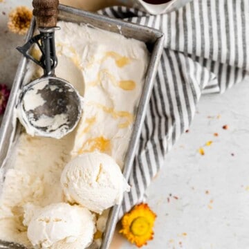 a tin filled with no churn honey vanilla ice cream. it has 2 scoops of ice cream piled on on side with an ice cream scooper sitting in the ice cream