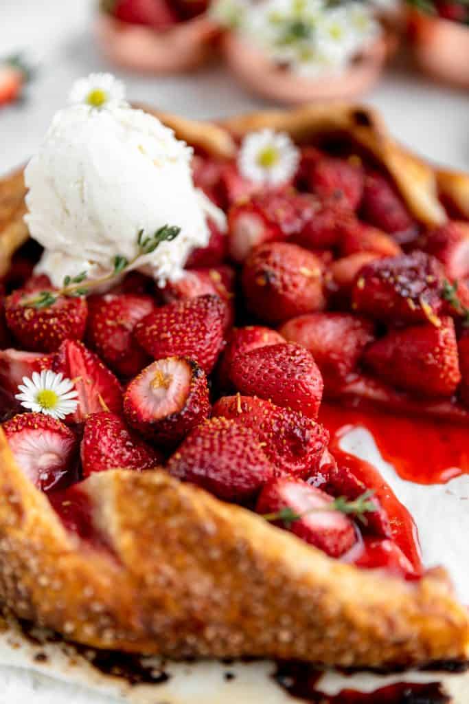 close up of the crust and strawberries of a cooked galette, garnished with honey vanilla ice cream and white daisies