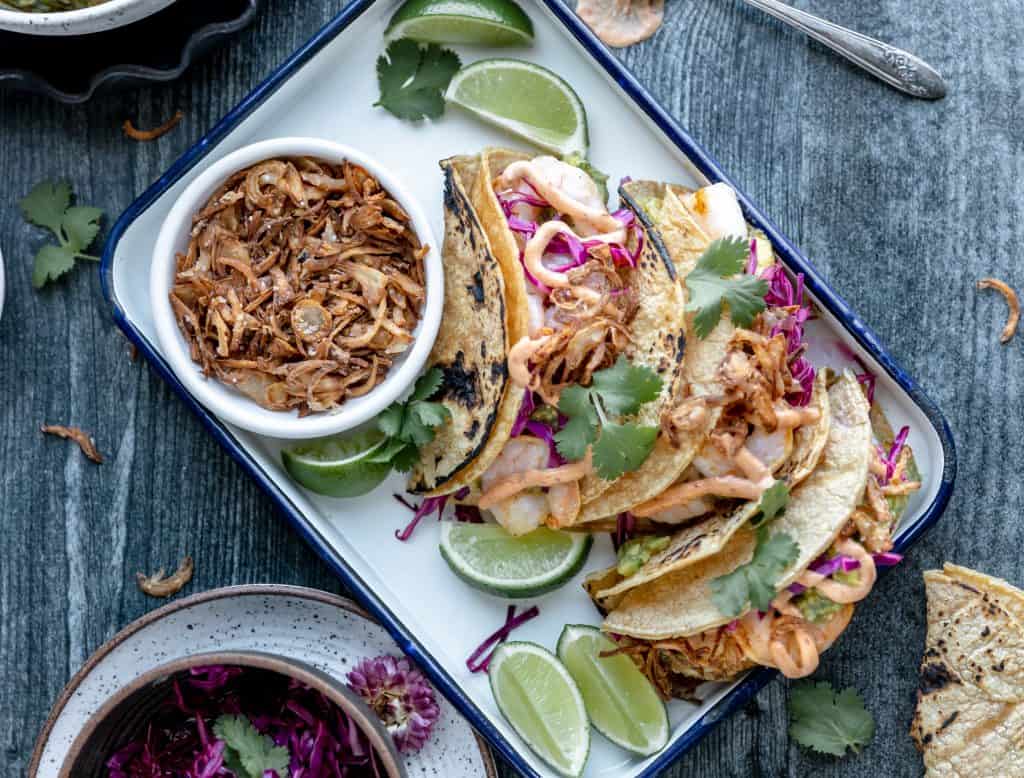 shrimp tacos with avocado relish and chipotle mayo on a tray with crispy fried shallots