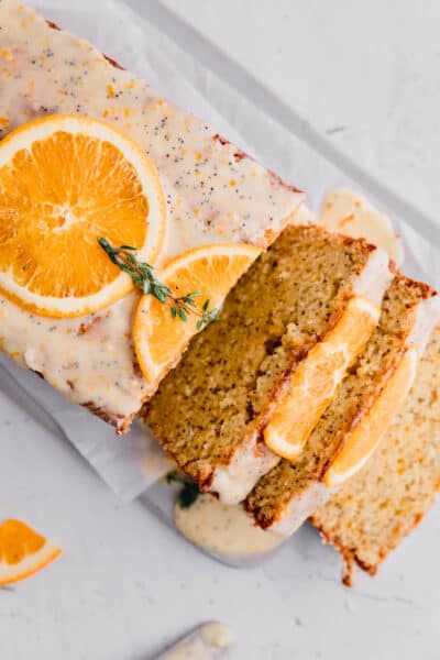 orange poppy seed bread with slices of fresh orange and thyme on top with a few slices lying to the side.