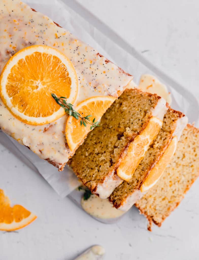 orange poppy seed bread with slices of fresh orange and thyme on top with a few slices lying to the side.