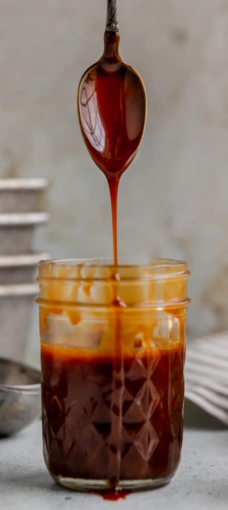 a jar of homemade caramel sauce  with a spoon above it drizzling caramel into the jar