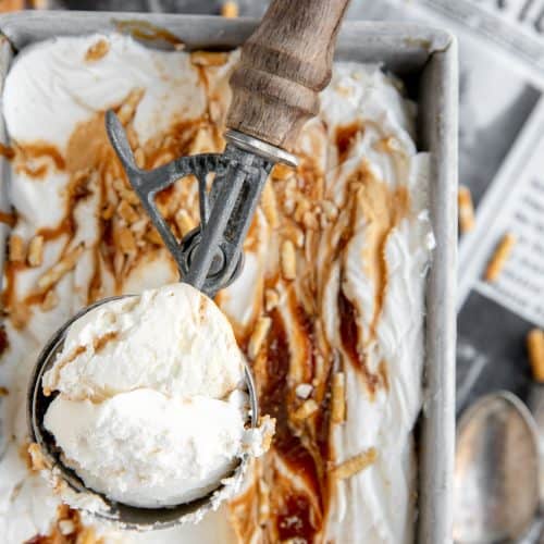 no churn salted caramel pretzel ice cream with a full ice cream scoop sitting in the tin