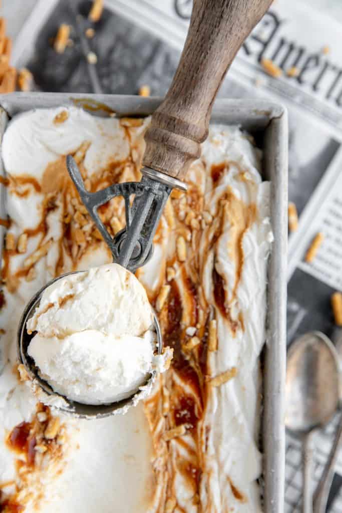 no churn salted caramel pretzel ice cream with a full ice cream scoop sitting in the tin