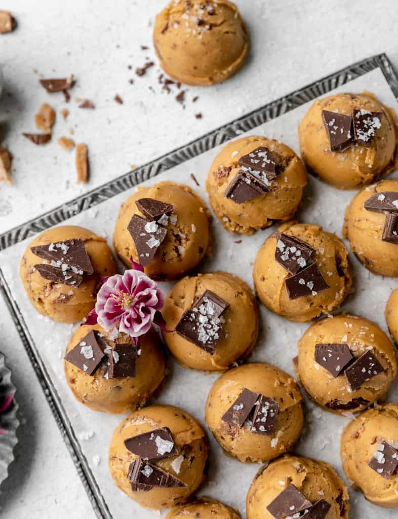 brown butter toffee chocolate chip cookies lined up on a sheet tray with flaky sea salt and a purple flower on top