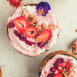 strawberry banana smoothie bowls served inside coconut shells with freeze dried strawberry and dragon fruit, granola and chia seeds