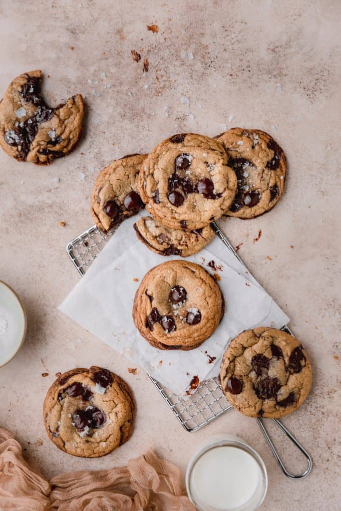 brown butter toffee chocolate chip cookies spread out on a rack topped with salt