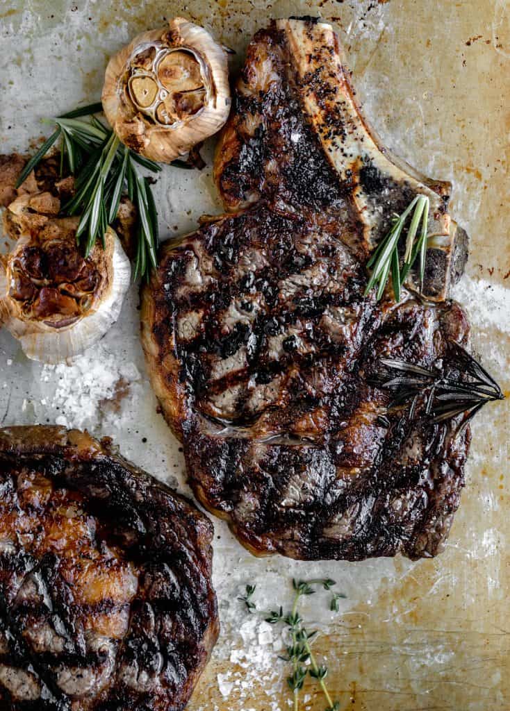 grilled steaks on a tray with roasted garlic heads