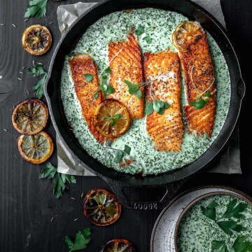 Salmon in a cast iron skillet with a creamy coconut schug sauce and roasted lemons