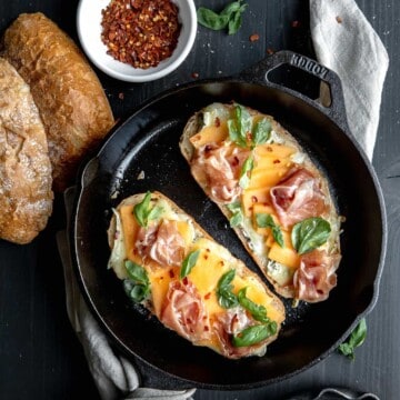 Prosciutto and melon panini topped with hot honey, chile flakes and brie cheese in a cast iron skillet