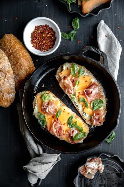 Prosciutto and melon panini topped with hot honey, chile flakes and brie cheese in a cast iron skillet