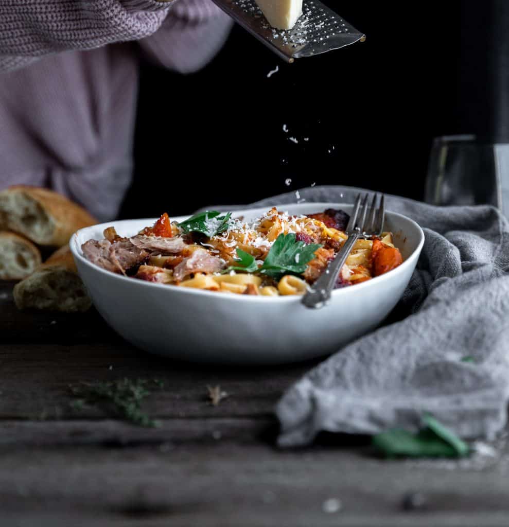 parmesan cheese being shredded over the top of a bowl of pork sugo and pasta