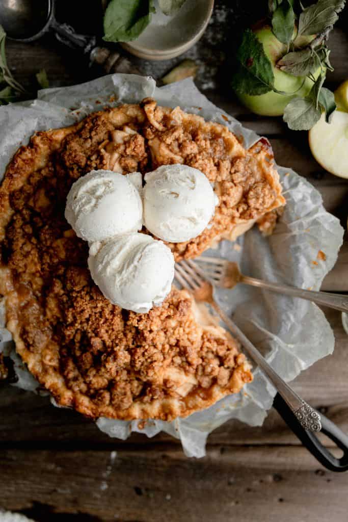 overhead shot of apple pie in a cast iron skillet topped with scoops of vanilla ice cream 