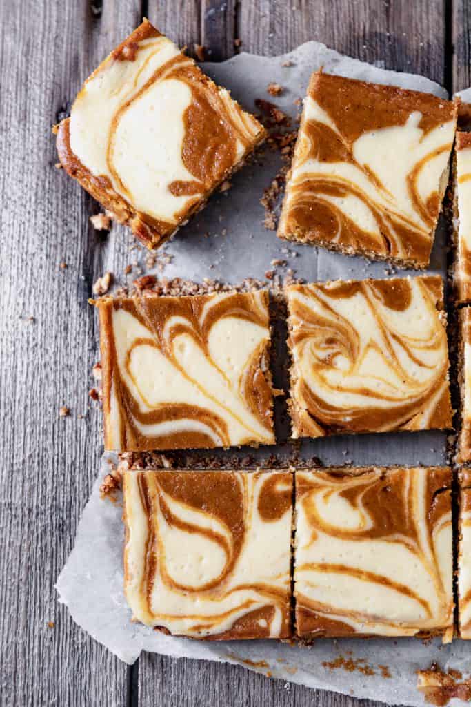 pumpkin swirl cheesecake bars cut into squares on top of parchment paper