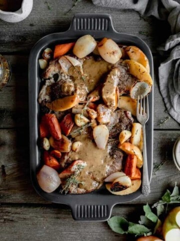 a serving platter with seared pork steaks, braised veggies and apples and bourbon cream sauce