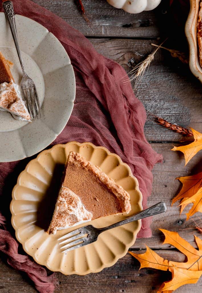 a slice of pumpkin pie on a plate with a fork and fall colored leaves surrounding it