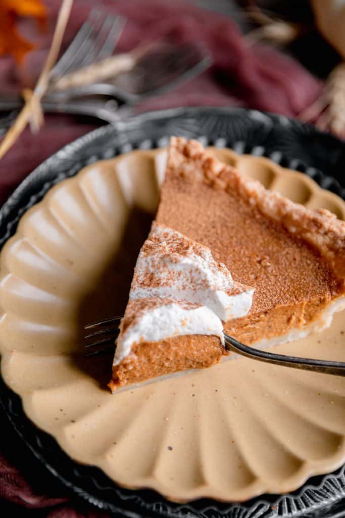 a slice of perfectly spiced pumpkin pie on a yellow plate with a fork going through the slice