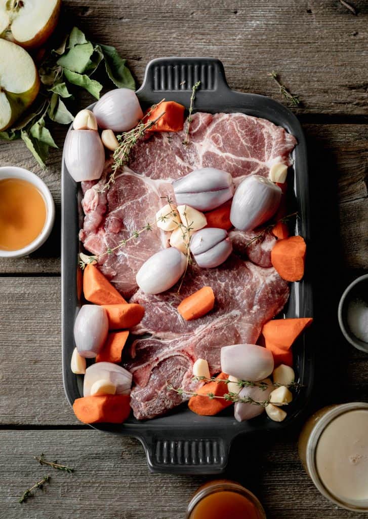 raw pork steaks on a platter with shallots, carrots, garlic and thyme