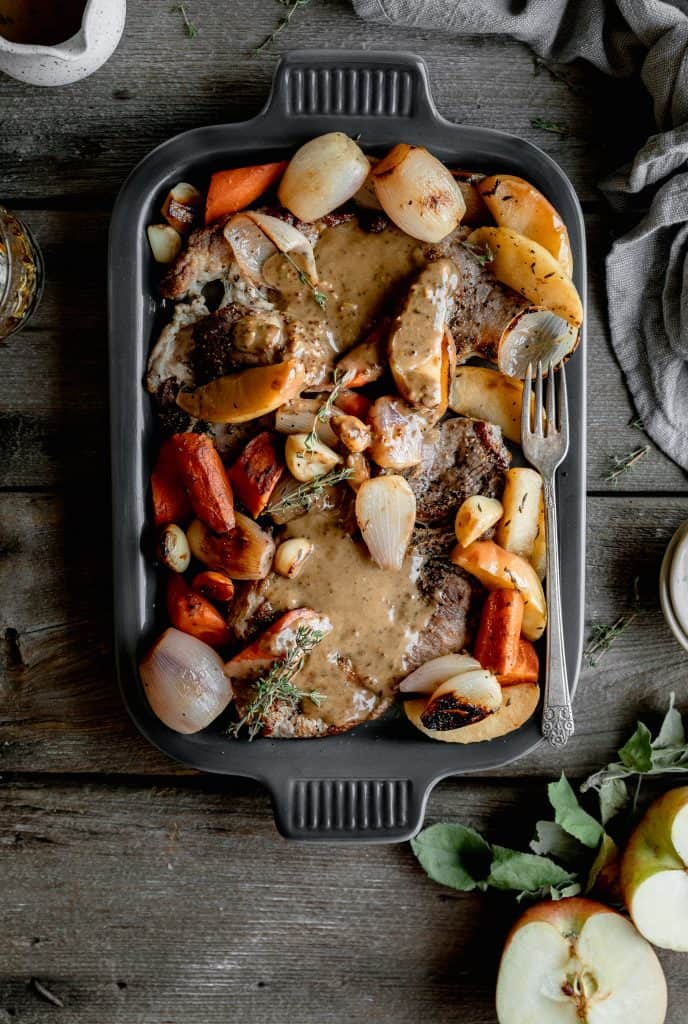 a serving platter with seared pork steaks, braised veggies and apples and bourbon cream sauce