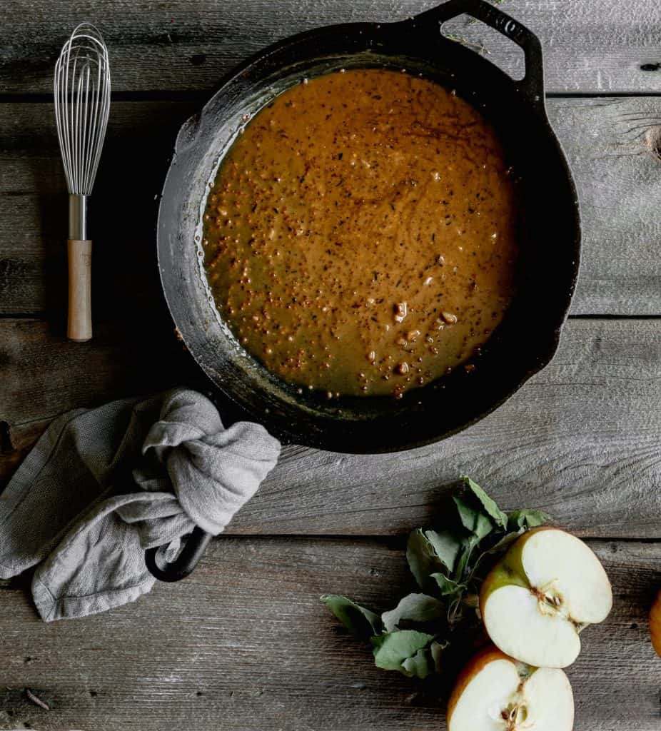 bourbon cream sauce in a cast iron skillet with a whisk and apples next to it