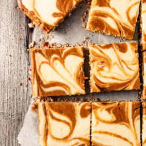 Pumpkin Swirl Cheesecake Bars cut into squares on top of parchment paper.