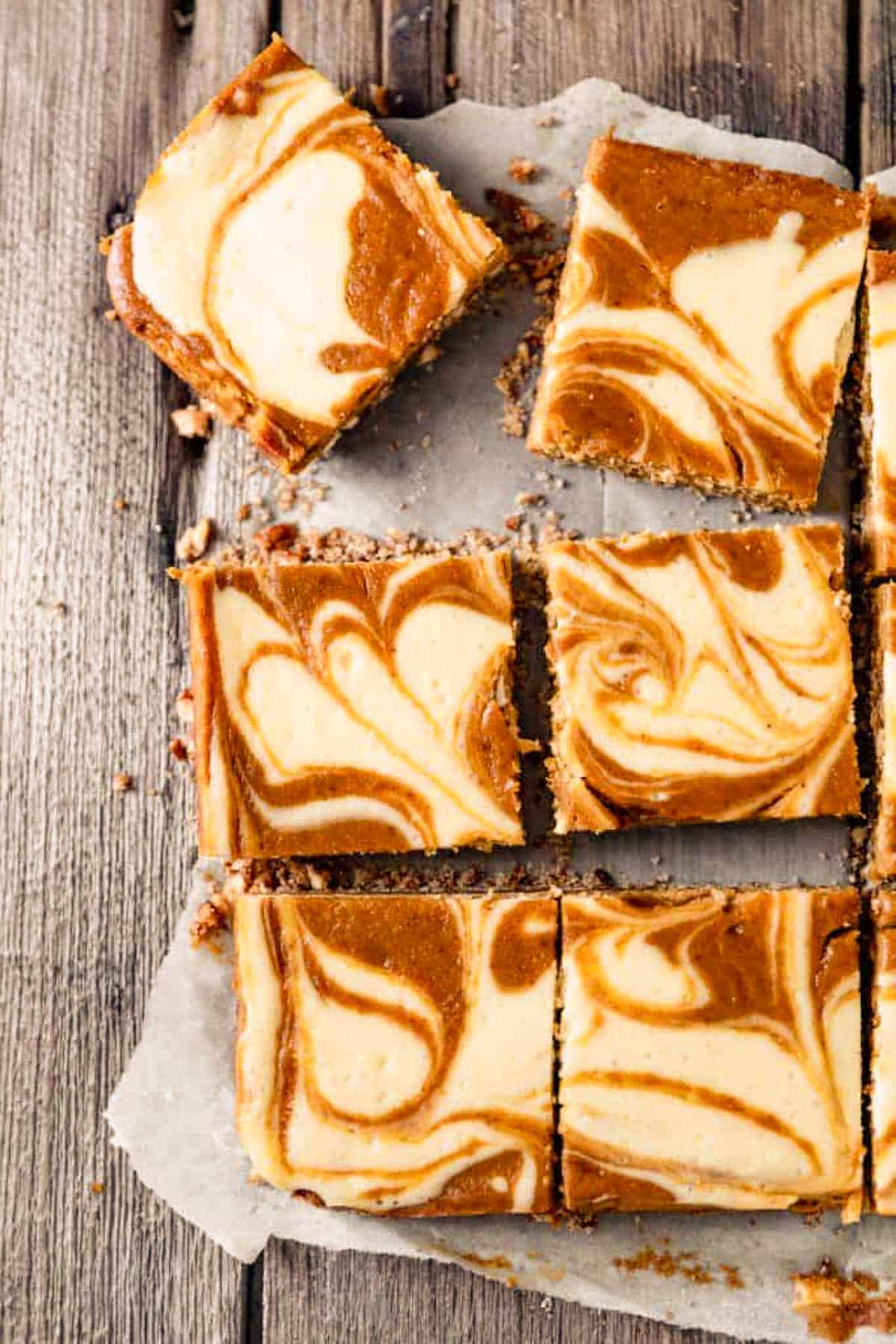 Pumpkin Swirl Cheesecake Bars cut into squares on top of parchment paper. 