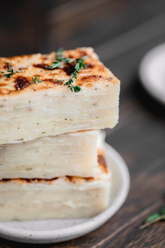 a stack of sliced au gratin potatoes where you can see all the layers, topped with fresh thyme