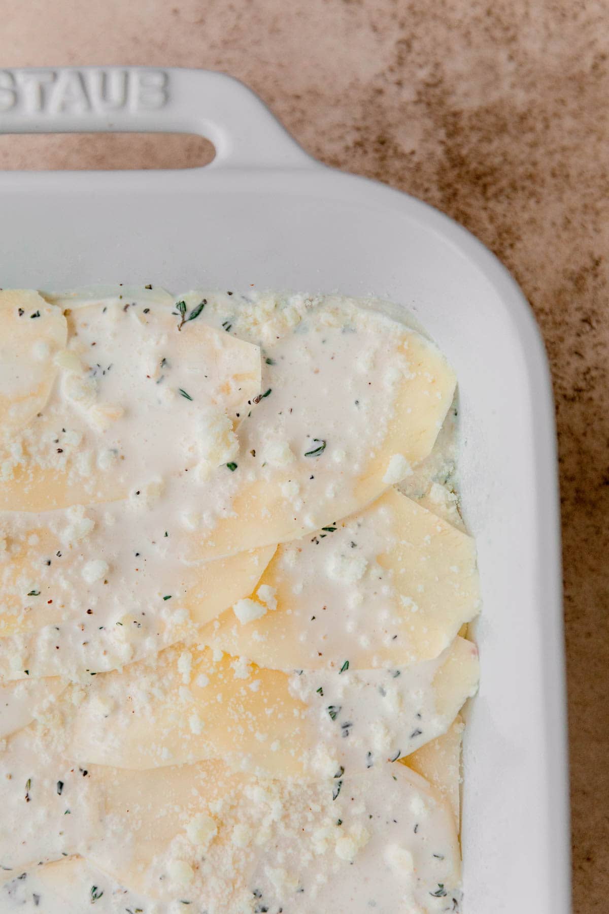 Potatoes, cream sauce and cheese being layered into a baking dish. 