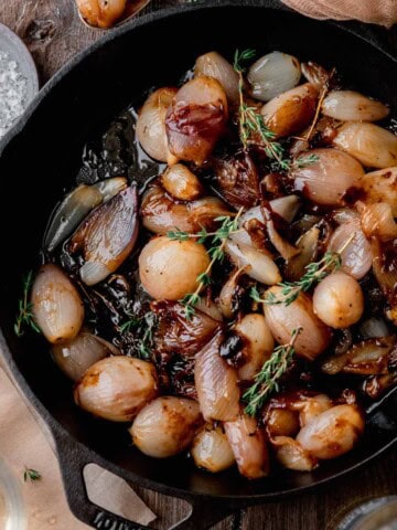 Glazed Shallots topped with fresh thyme in a cast iron skillet.