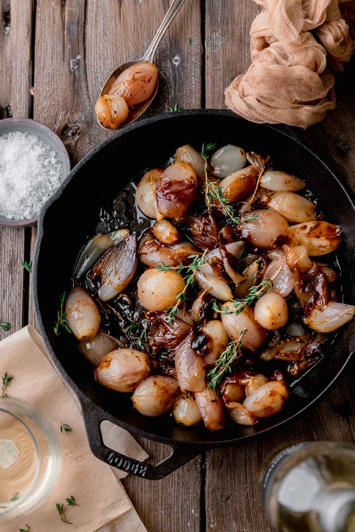 Glazed Shallots topped with fresh thyme in a cast iron skillet. 