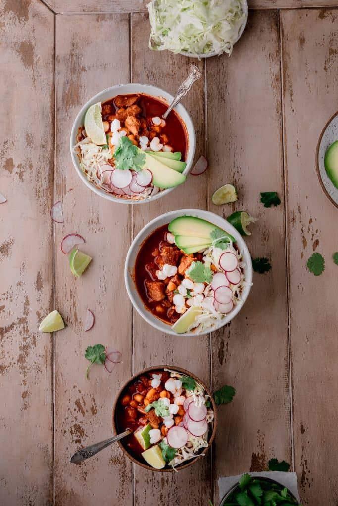 3 bowls of pozole with cabbage, radish, lime, avocado and cilantro