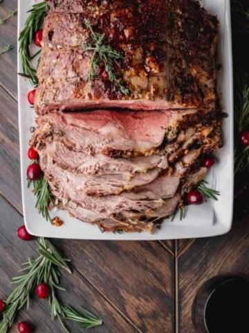 sliced standing rib roast with red wine demi glace in a dish to the side